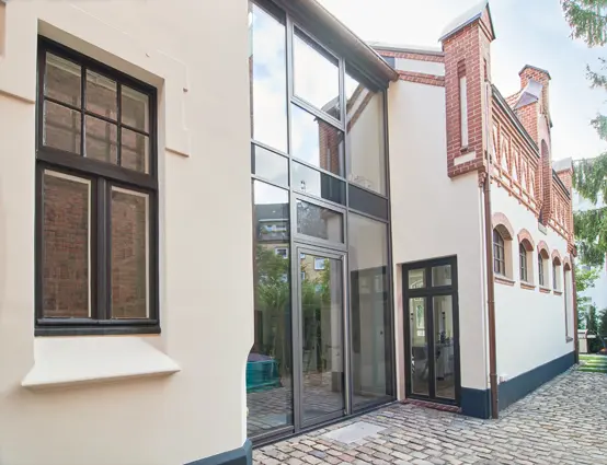 Modernes Gebäude mit großen Glasfenstern und Ziegelsteinakzenten, mit Kopfsteinpflaster und einer Mischung aus modernen und klassischen architektonischen Stilen.