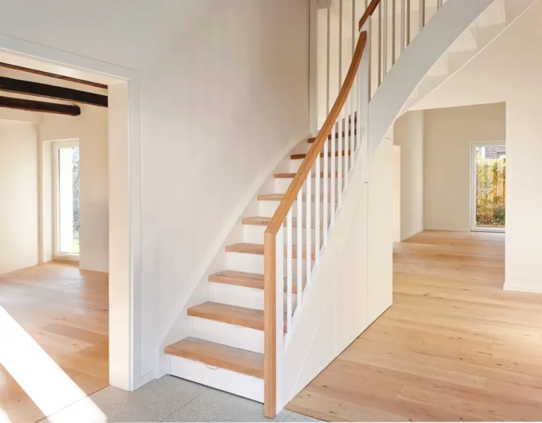 Das moderne, helle Interieur von Architekten Altbausanierung zeichnet sich durch eine Holztreppe mit weißem Geländer, helle Holzböden, luftige weiße Wände und große Fenster aus, die den Raum mit natürlichem Licht durchfluten.